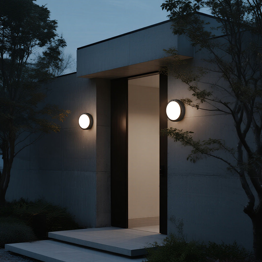 Contemporary home entryway illuminated by a pair of sleek round outdoor wall lights on a concrete wall.