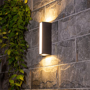 Vertical LED wall sconce mounted on textured stone exterior creating ambient lighting