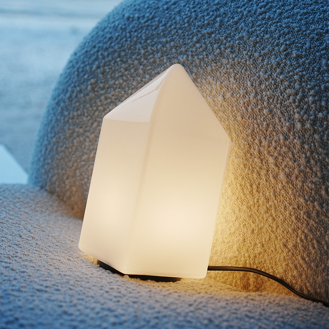 Contemporary house-shaped modern white table lamp with warm glow on gray sofa.