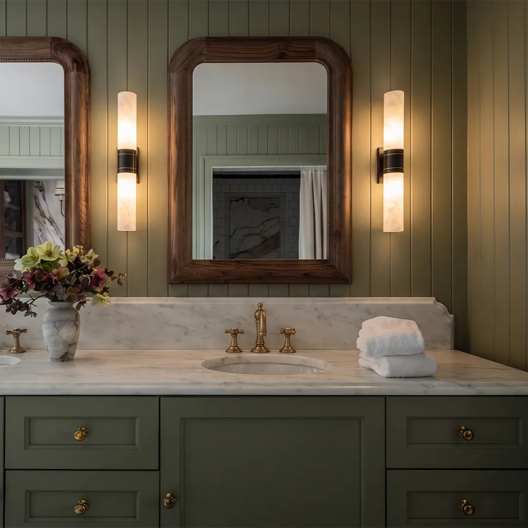 Contemporary indoor wall sconces flanking a bathroom mirror with elegant stone-look shades and warm lighting.