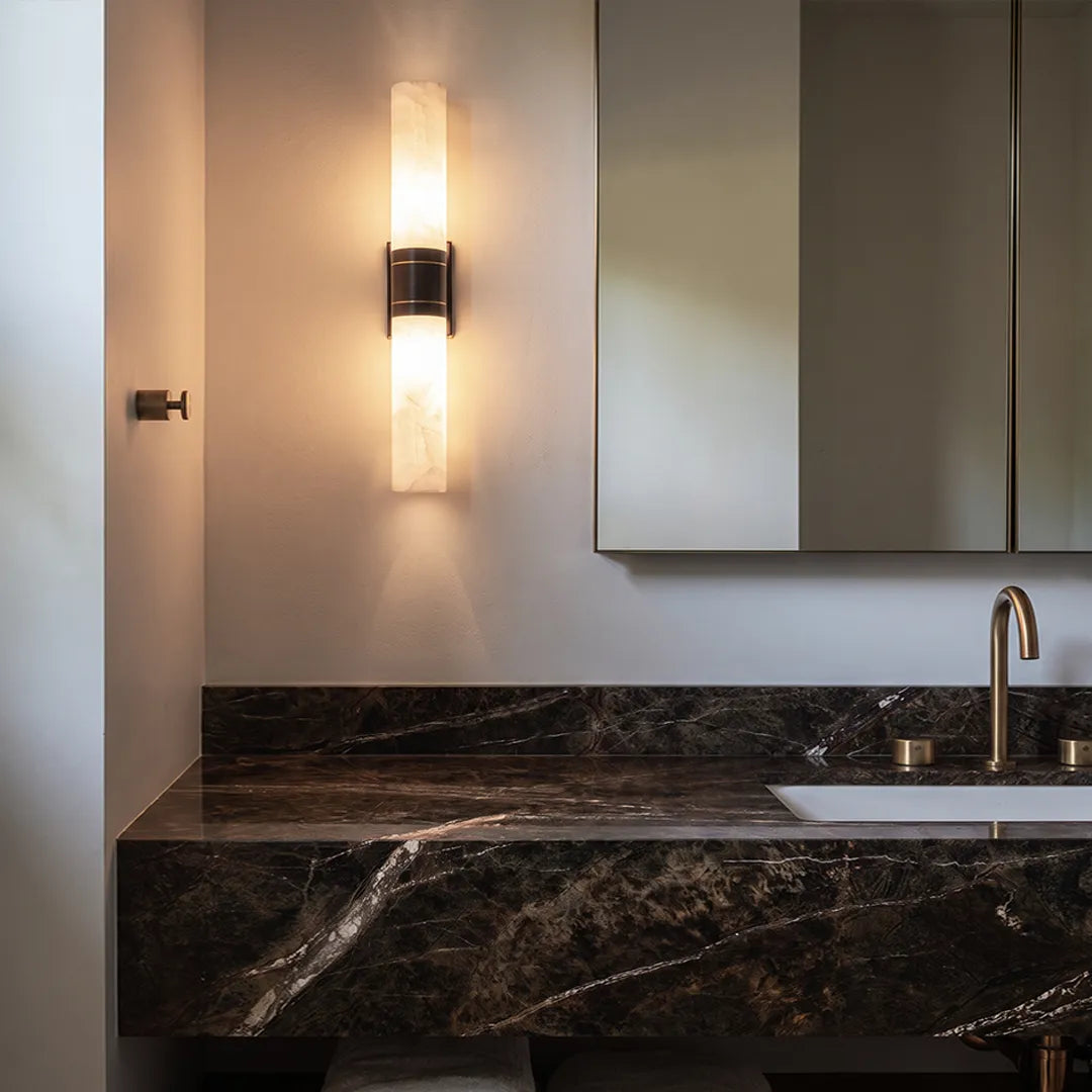 Contemporary indoor wall sconces mounted above a black marble vanity with a refined vertical design and warm light.