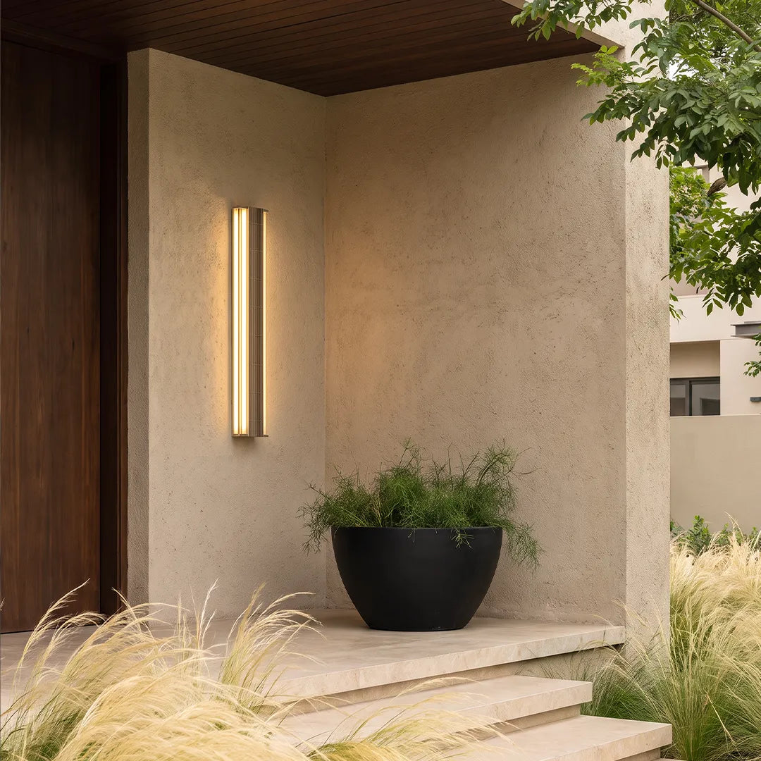 Contemporary LED wall light mounted near a covered porch entry with a planter and warm vertical illumination.