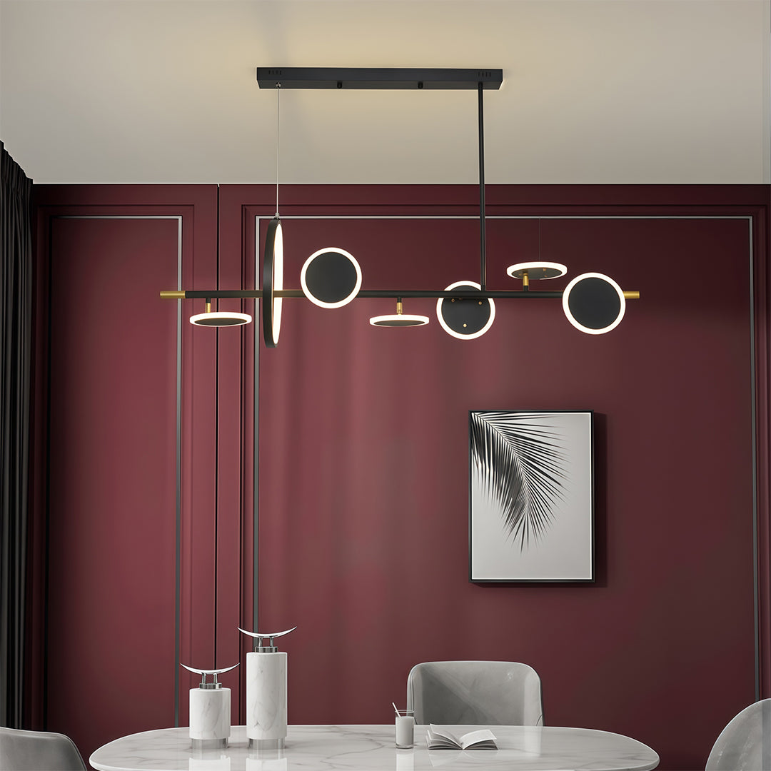 Contemporary 6 light chandelier with a linear design and adjustable rings, placed above a large table in a red-toned room.