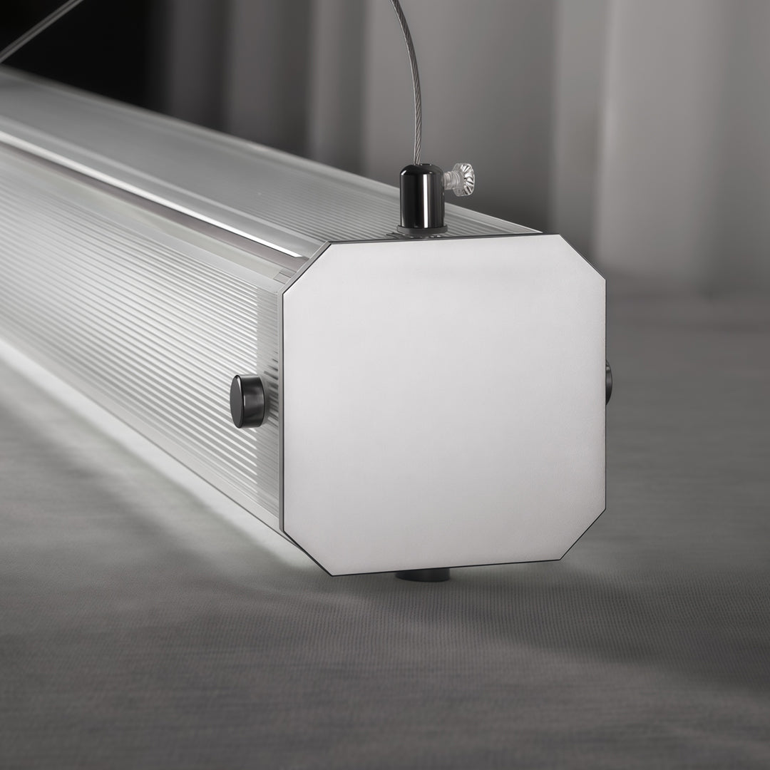 Detailed view of contemporary linear suspension lighting with geometric end cap and suspended cable mounting.