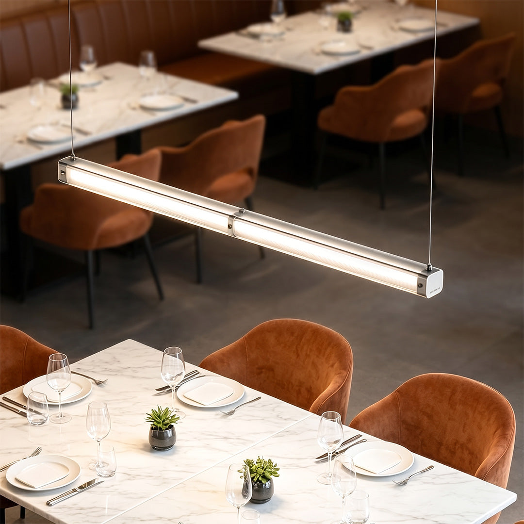 Contemporary linear suspension lighting hanging above restaurant dining tables with warm ambient illumination.