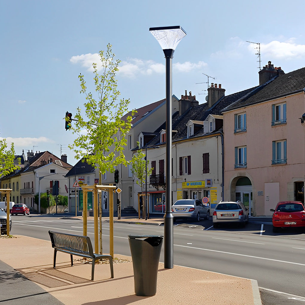 Contemporary night street light installed along a small city square with benches and trees.