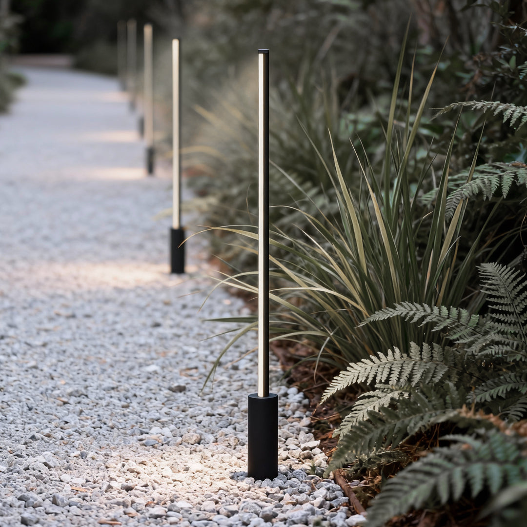 Contemporary outdoor floor lamps arranged along a gravel garden path with plants.