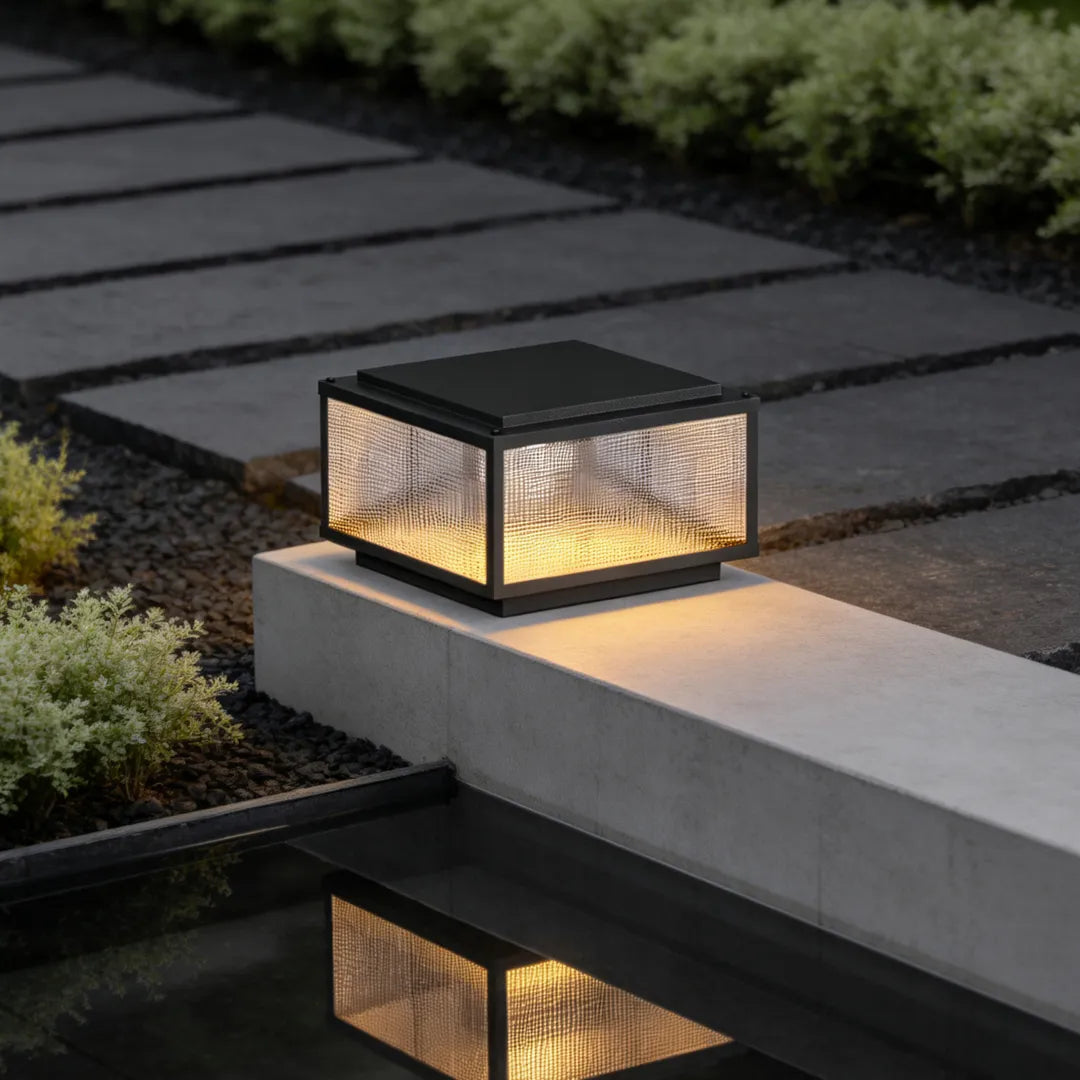 Contemporary outdoor pillar light fixture illuminating a low concrete wall along a stepping stone walkway.