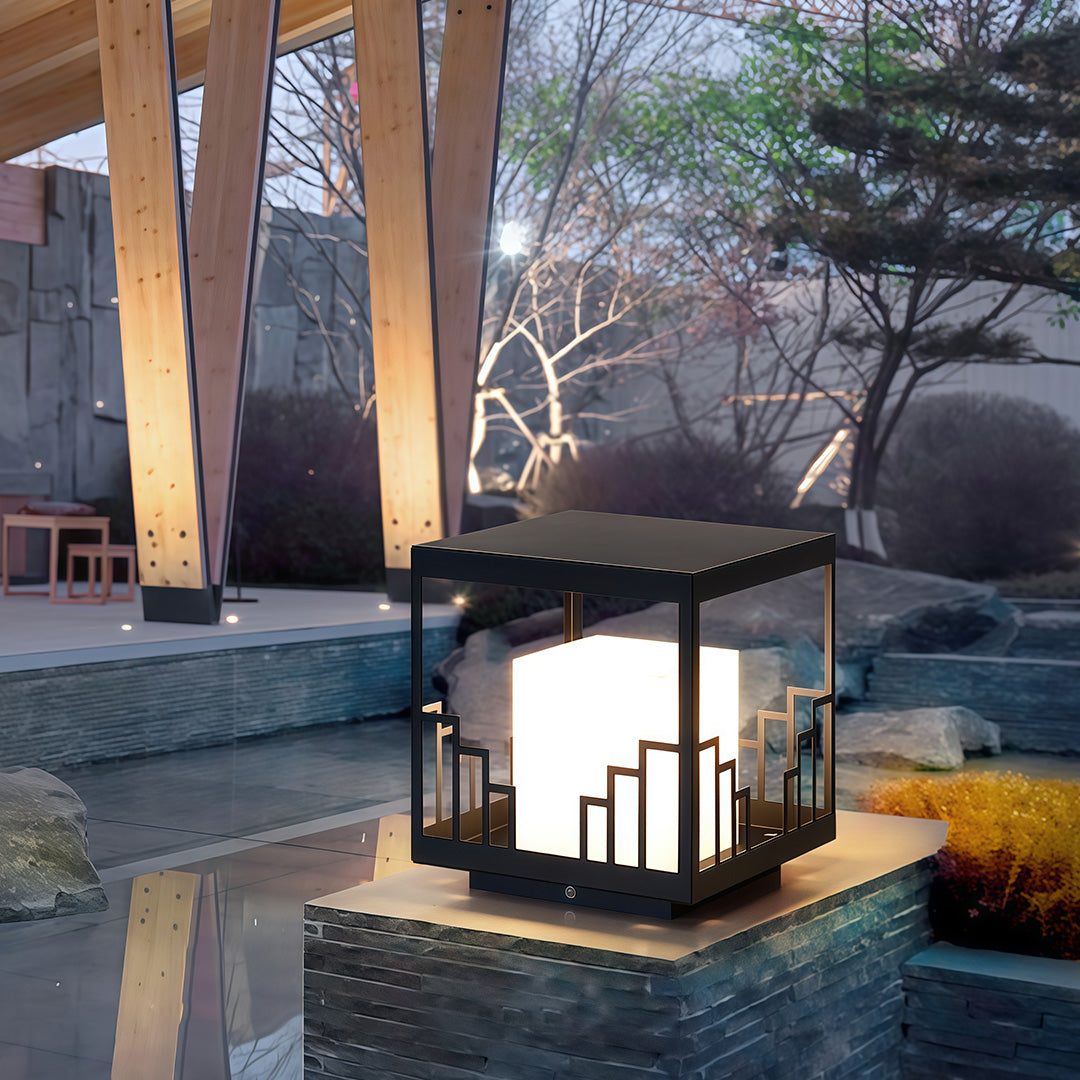 Contemporary outdoor pillar light with glass shade chandelier design providing decorative accent lighting on stone wall feature.