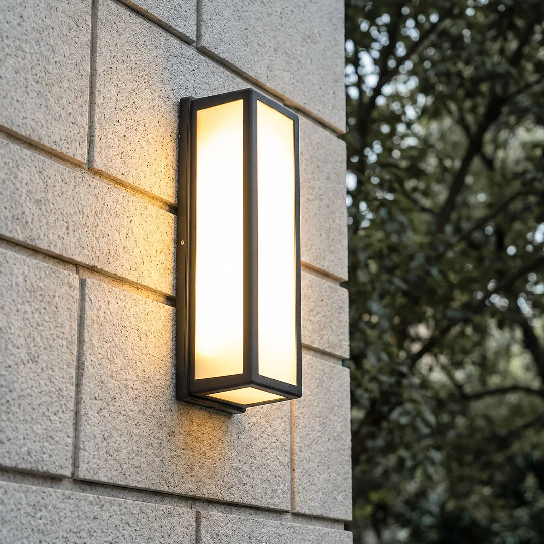Contemporary outdoor wall light mounted on a textured stone exterior wall with a slim rectangular black frame.