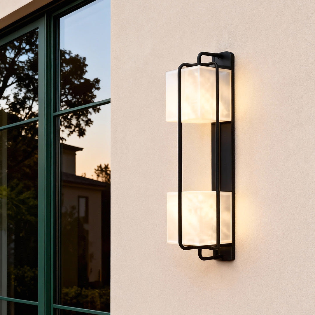 Contemporary outdoor wall lighting installed on beige exterior wall beside tree and doorway