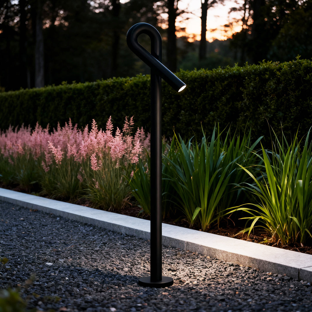 Contemporary outdoor wall lighting bollard light post illuminating garden pathway with pink flowers at dusk
