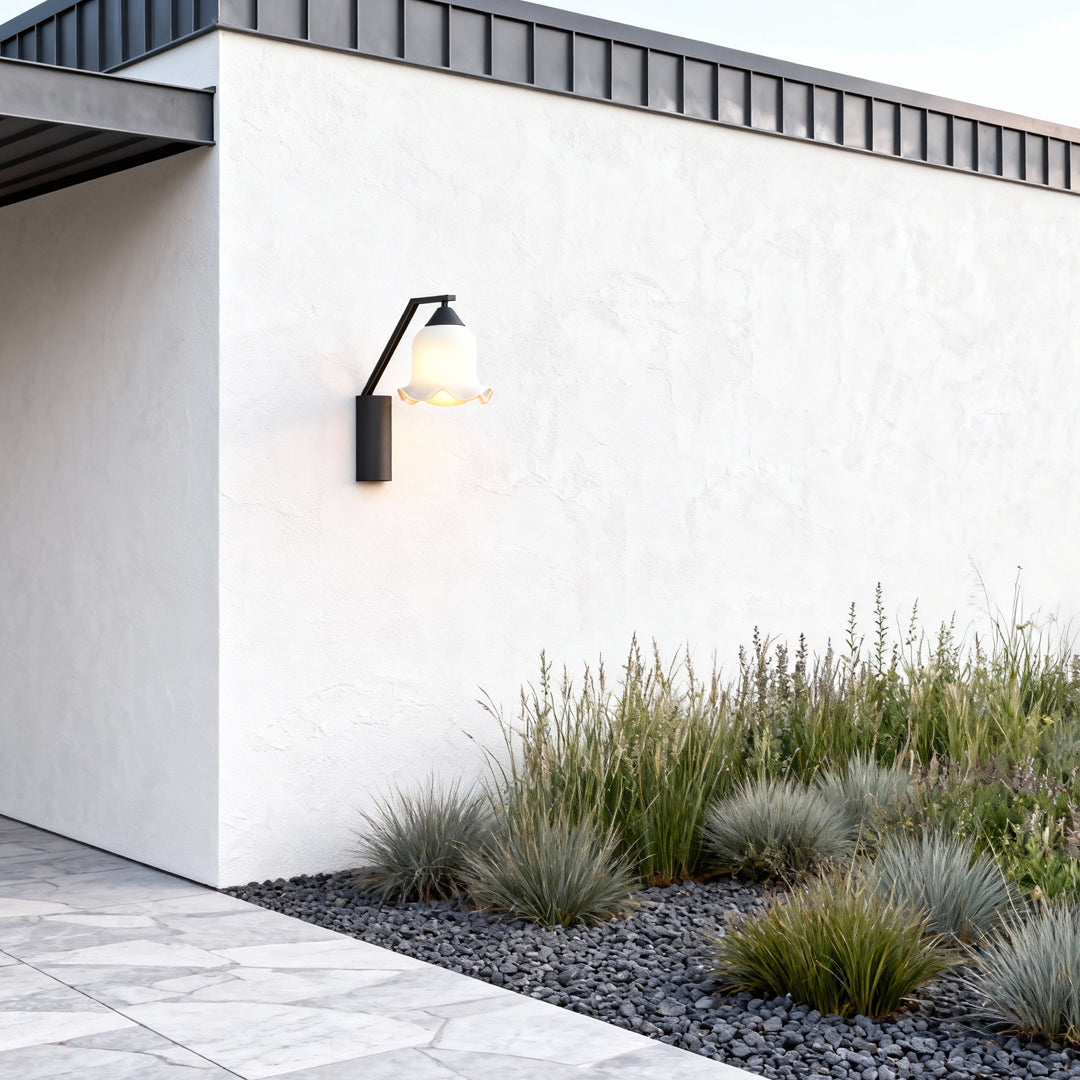 Contemporary outdoor wall lighting flower wall sconce mounted on white exterior wall beside modern landscaping and gravel