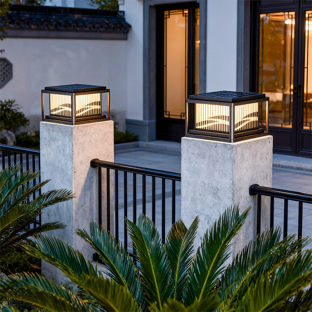 Contemporary pillar lights positioned on textured stone posts near modern white house with glass doors.