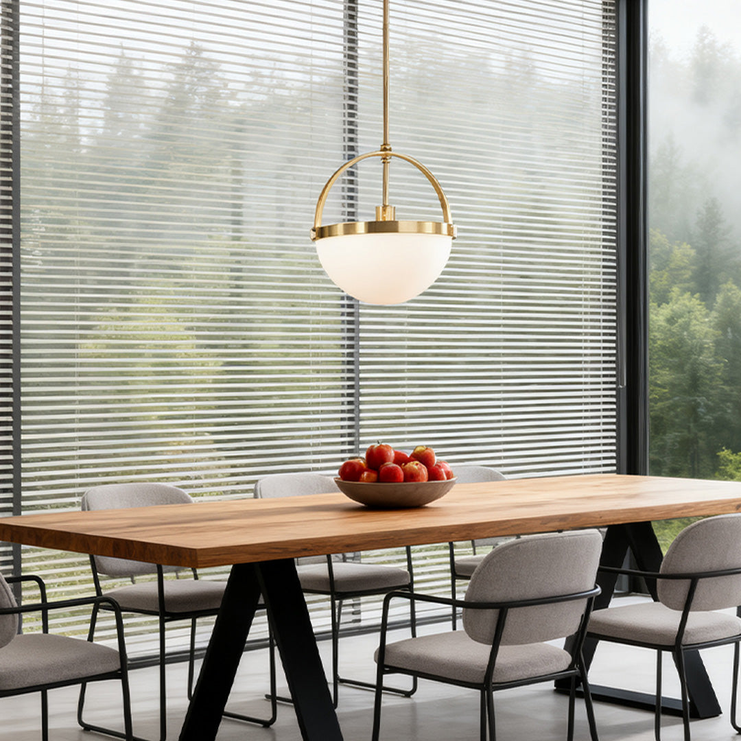 Contemporary gold and white pendant light with a semi-globe opal shade, hanging over a large wooden dining table with a scenic window view.