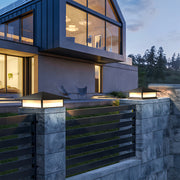 Contemporary black pillar lights with sloped roof mounted on a textured stone fence outside a modern home.