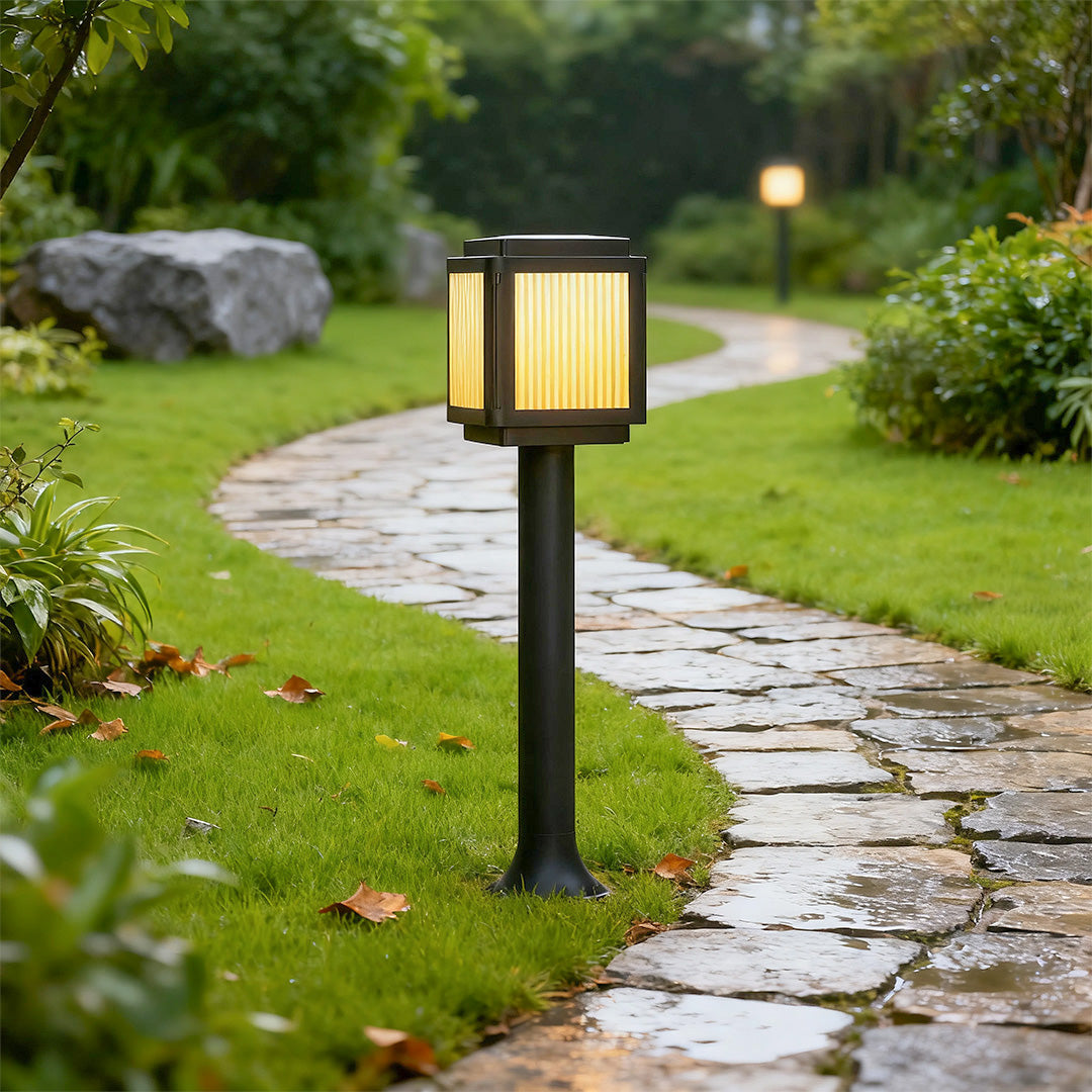 Contemporary solar path light installed along a stone pathway in a garden, providing warm illumination.
