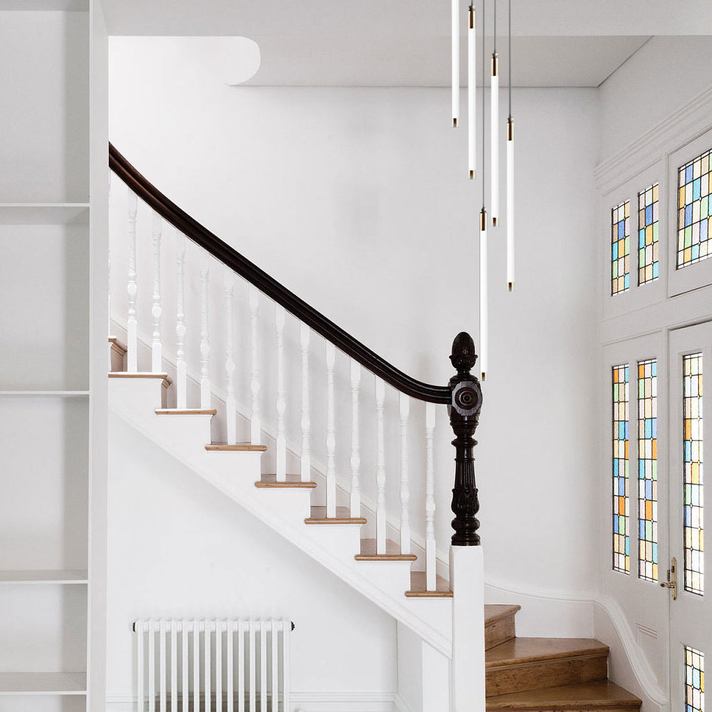 Contemporary staircase chandelier with linear pendant lights, enhancing a white staircase's elegance.