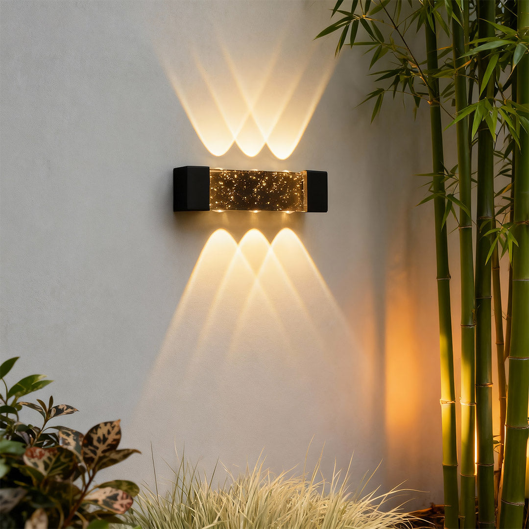Contemporary up down wall light featuring glass shade chandelier styling creating dramatic bidirectional illumination beside bamboo plant.