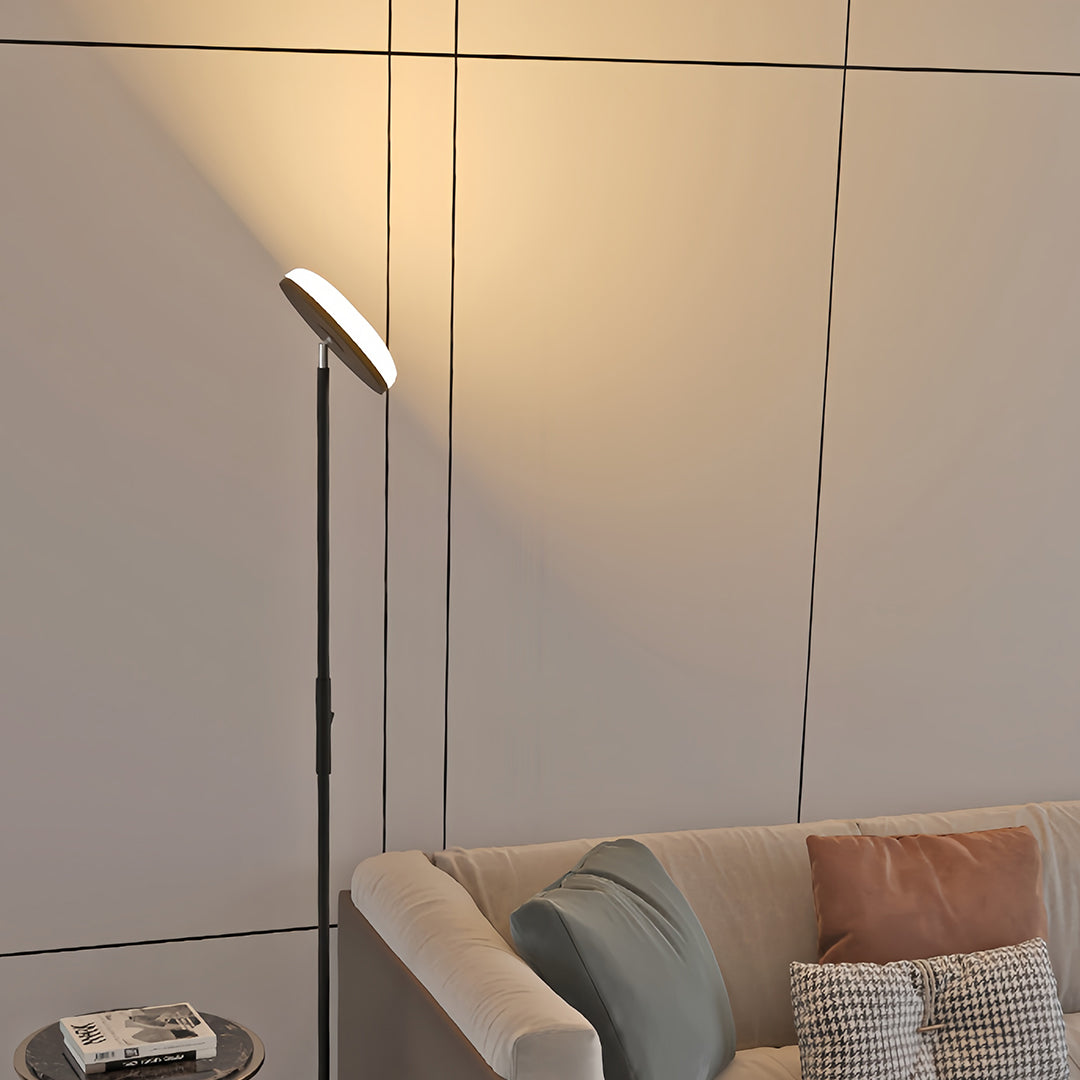 Modern uplight floor lamp with sleek black pole and circular LED top providing ambient ceiling illumination