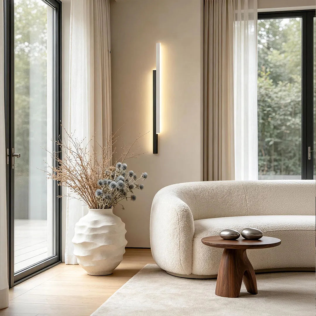 Contemporary vertical wall light beside a window and curved lounge chair in a bright sitting area.