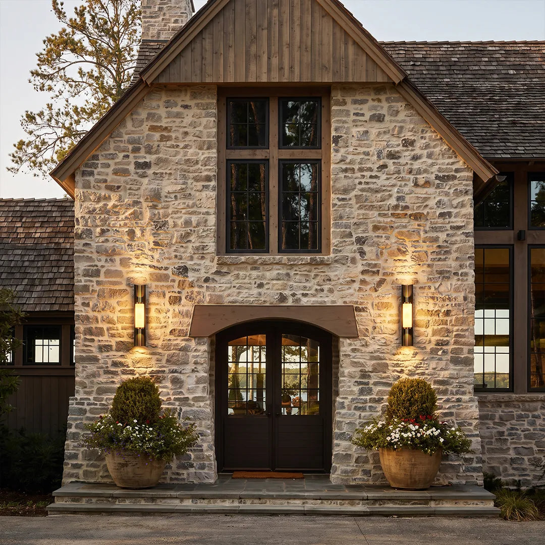 Contemporary wall light fixtures flanking the entrance of a rustic stone house for balanced exterior lighting.