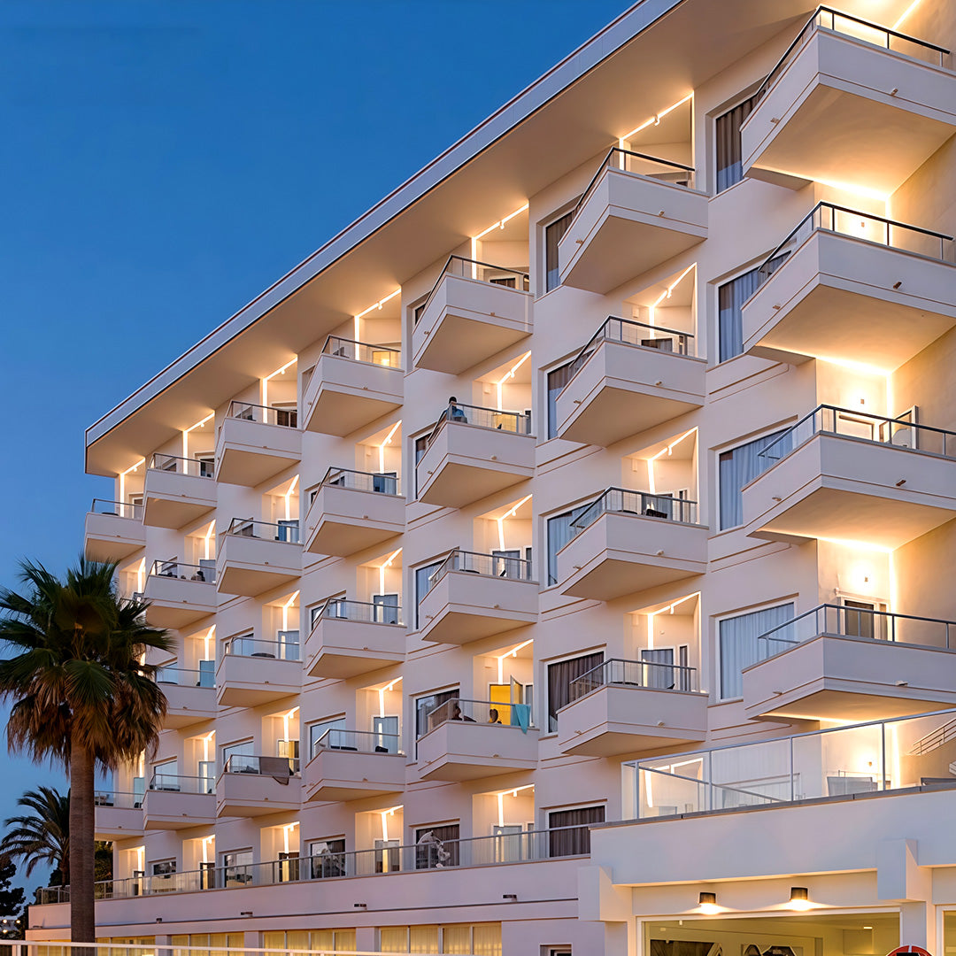 Contemporary white outdoor wall lights featuring glass shade chandelier styling illuminating modern hotel building facade at dusk.