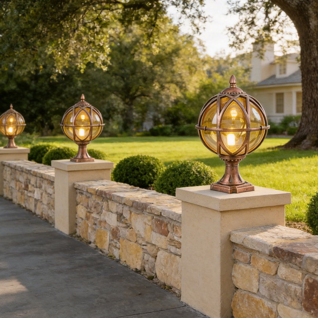 Copper globe pillar lights on stone wall posts lining a green park driveway in the morning sun.