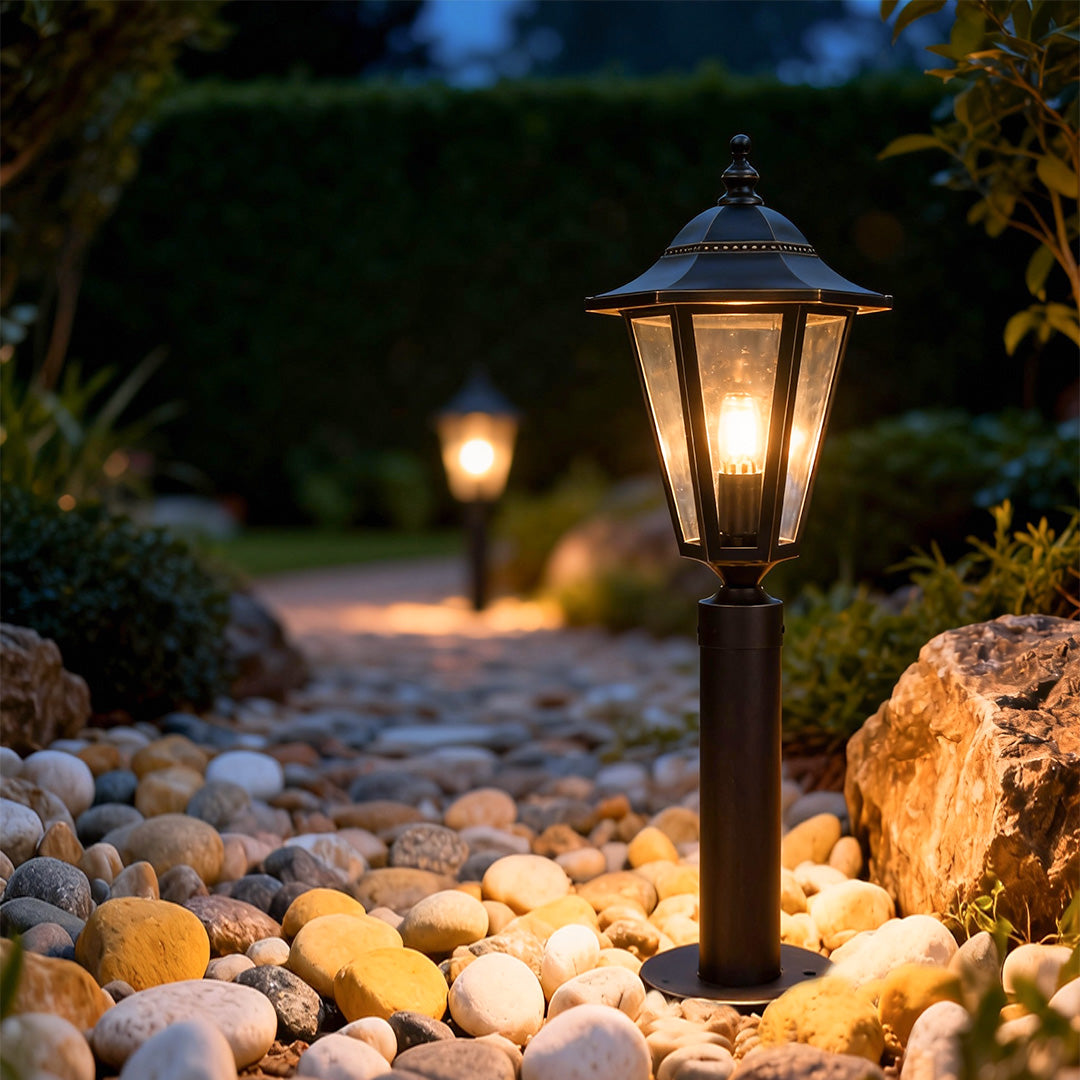Copper landscape path lights installed along a garden walkway, casting warm light over stones and surrounding greenery at night.