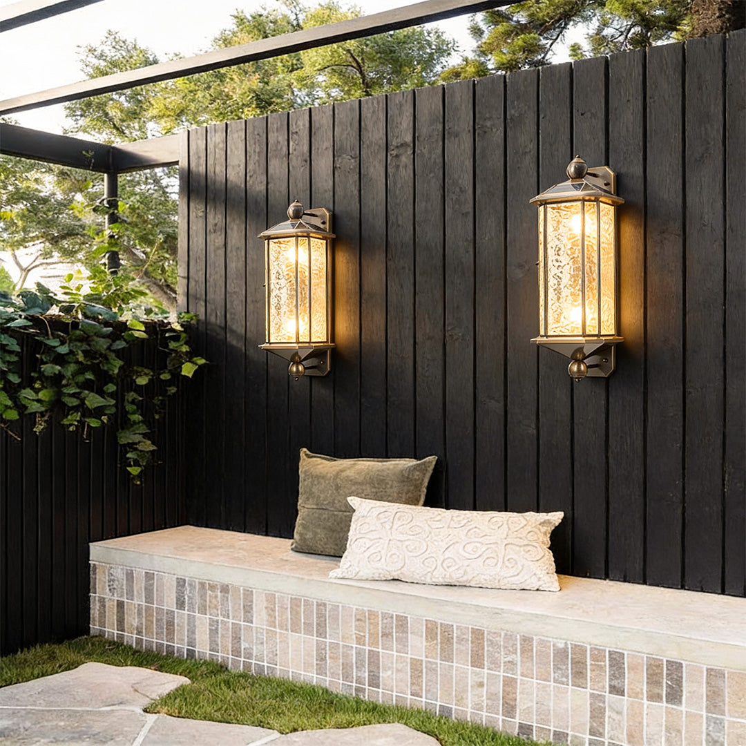 Pair of copper outdoor wall lantern fixtures mounted on a dark fence, creating cozy ambient lighting for an outdoor seating area.