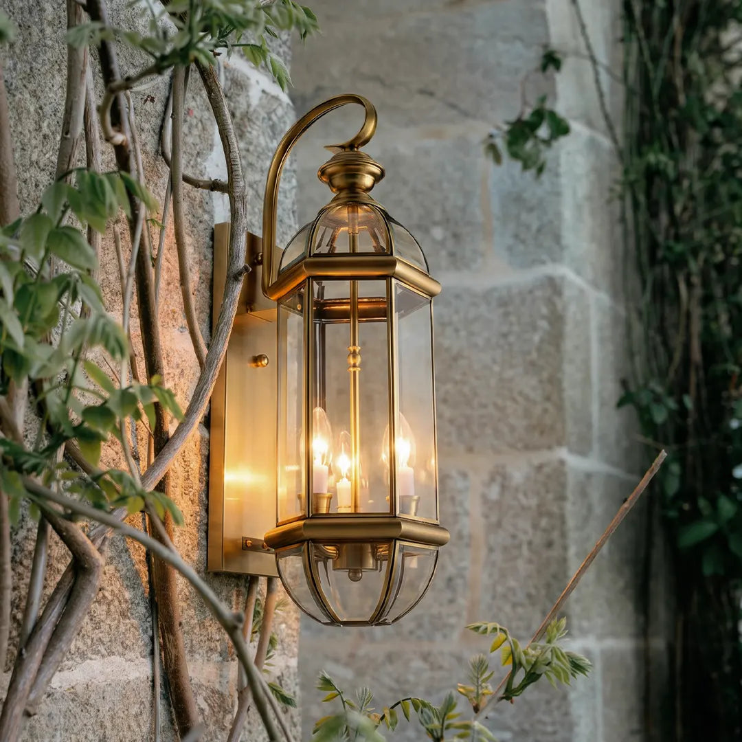 Copper outdoor wall sconce mounted on a stone wall, glowing warmly beside climbing greenery.
