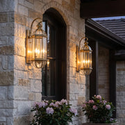 Copper outdoor wall sconce mounted beside a stone entry door, featuring a tall lantern design with warm glowing bulbs.
