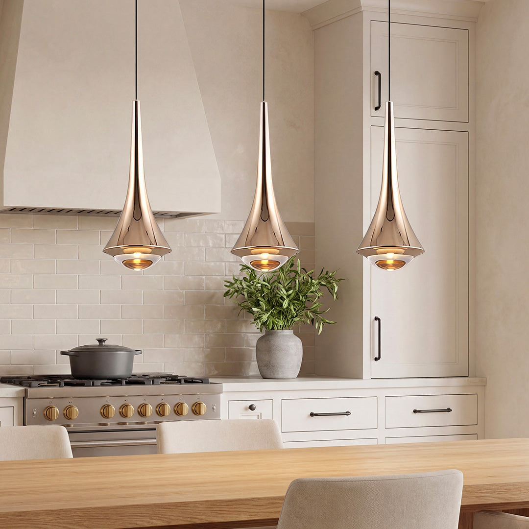 Trio of polished copper trumpet pendant lights over a white kitchen island and brick backsplash.