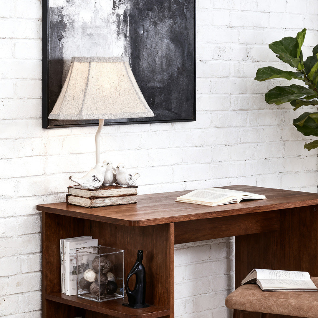 Country cottage style small bird table lamp on a rattan wicker nightstand beside a bed with blue patterned curtains and duvet.