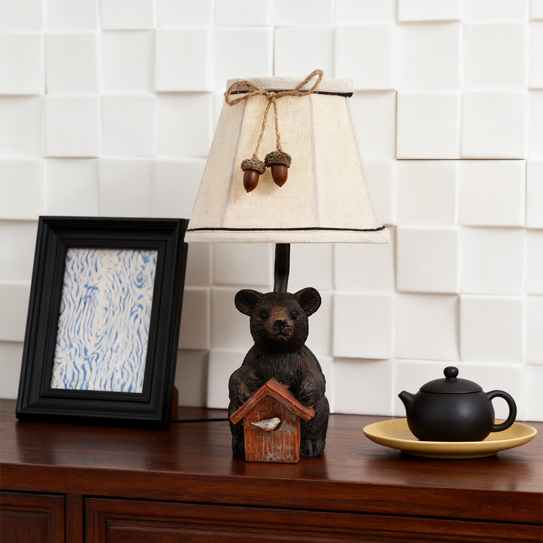 Bear table lamp with a country charm theme, set on a dark wood dresser next to a black picture frame and teapot against a tiled wall.
