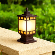 Craftsman metal pillar light with amber glass casting soft light on tan stone pier in green landscape
