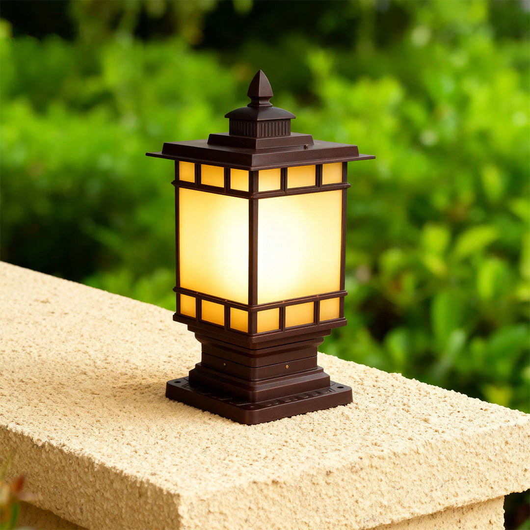 Craftsman metal pillar light with amber glass casting soft light on tan stone pier in green landscape