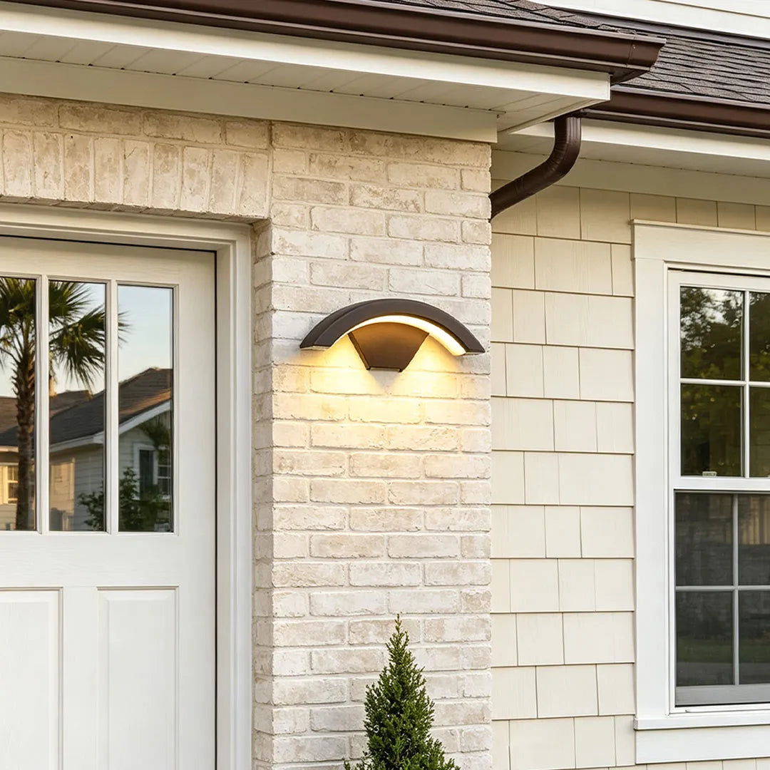 Creative moon curved wall sconce installed on a cream brick exterior beside a garage side door.