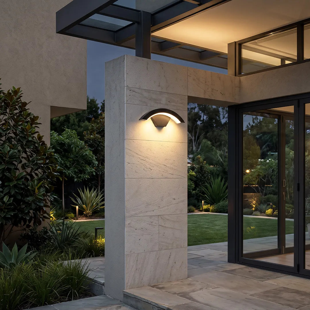 Creative moon curved wall sconce installed on a modern stone column outside a contemporary home.
