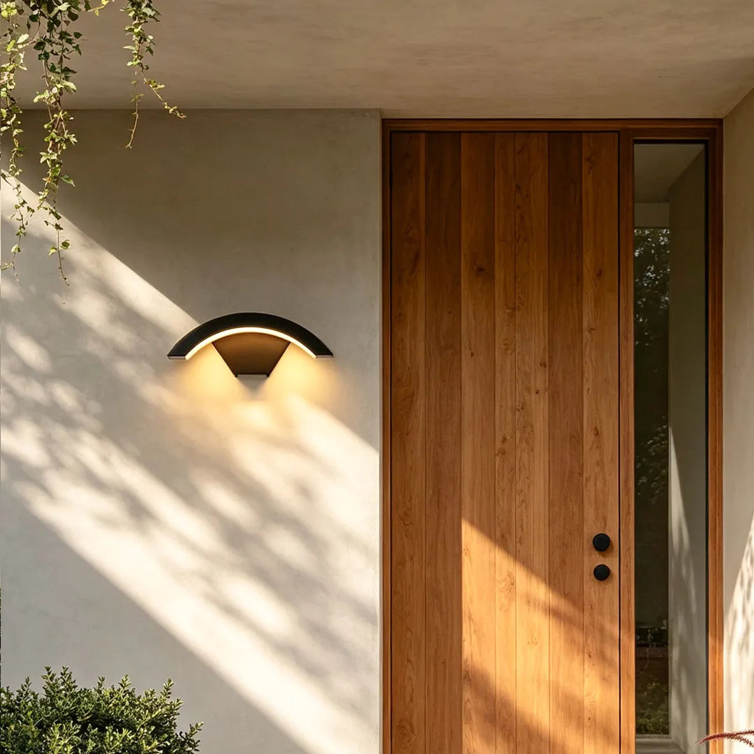 Creative moon curved wall sconce mounted on a light stucco wall beside a natural wood entry door.