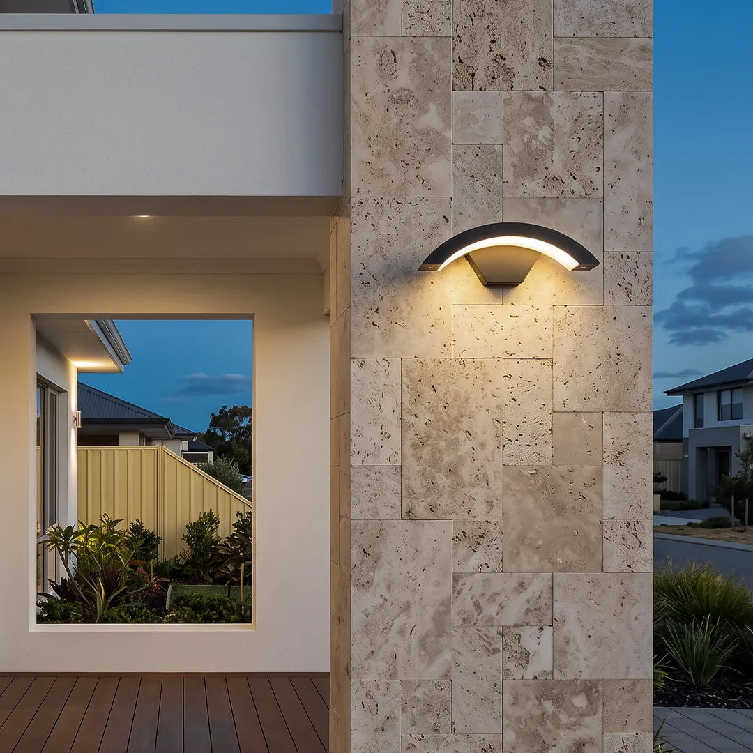 Creative moon curved wall sconce mounted on a travertine exterior wall beside a covered entryway.