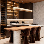 Contemporary crystal linear pendant light illuminating a marble kitchen island with warm metallic tones.