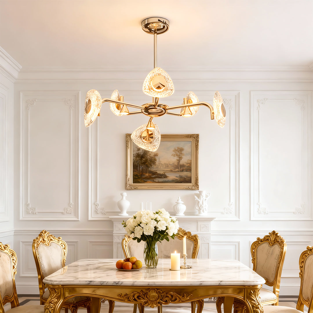 Crystal vintage chandelier suspended above ornate dining room with classical white molding and gold furniture accents