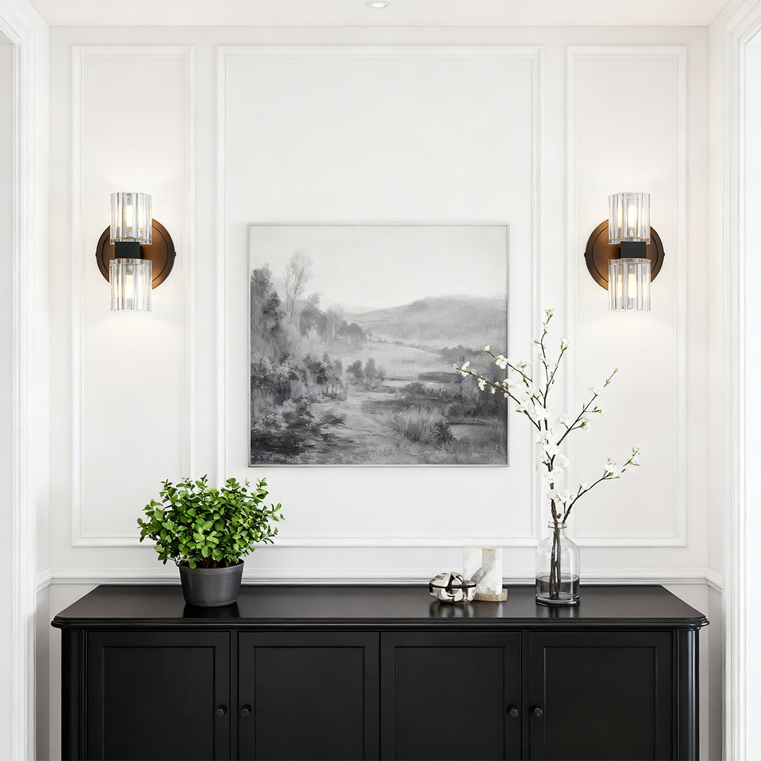 Crystal wall light pair flanking artwork above black console in minimalist white entryway