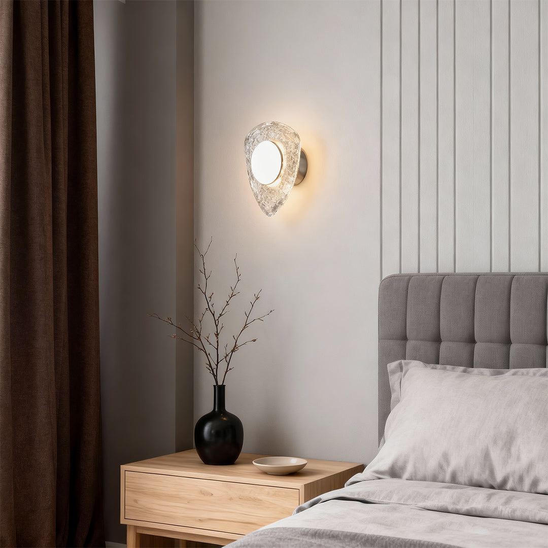 Crystal wall sconce light fixture illuminating bedroom with gray upholstered headboard creating ambient warm glow