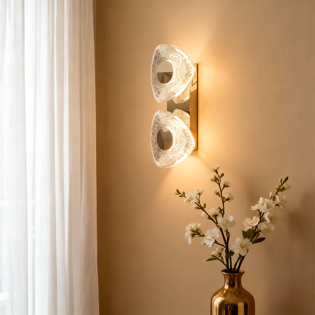 Crystal wall sconce light fixture providing elegant lighting on neutral wall beside decorative vase with branches