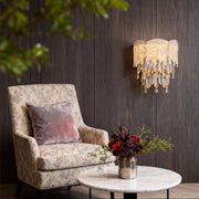 Cozy reading corner lit by crystal wall sconce lighting with gold frame and glass strands.