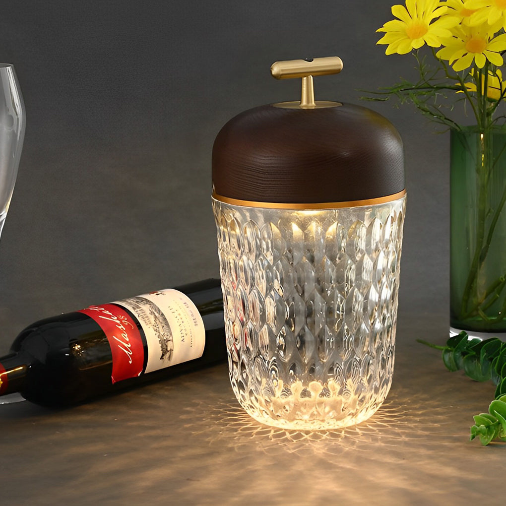 Sophisticated cup glass table lamp with a dark wooden top, placed beside a wine bottle and flowers.