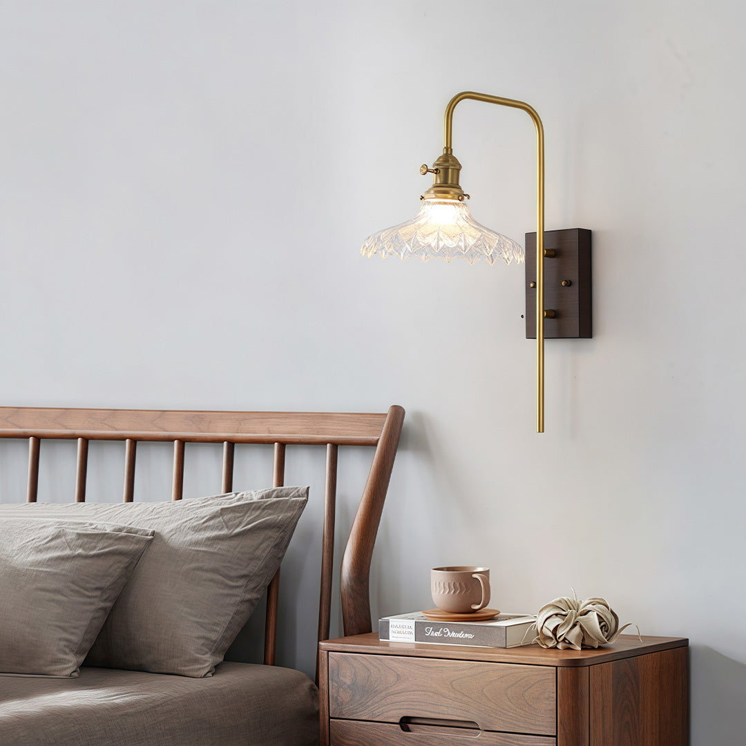 Curved gold-arm glass wall lights featuring a scalloped, clear glass shade, providing elegant task lighting in a bedroom.