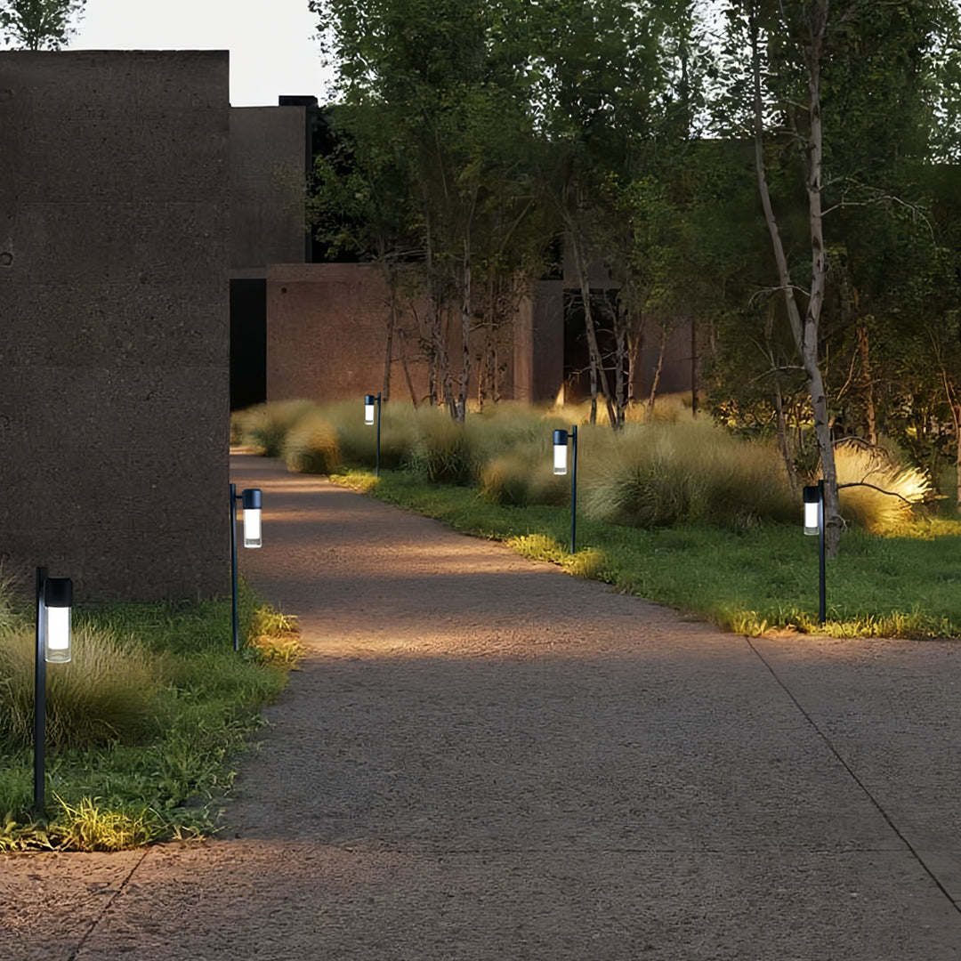 Warm contemporary path lights illuminating a curved gravel pathway in a landscaped backyard.
